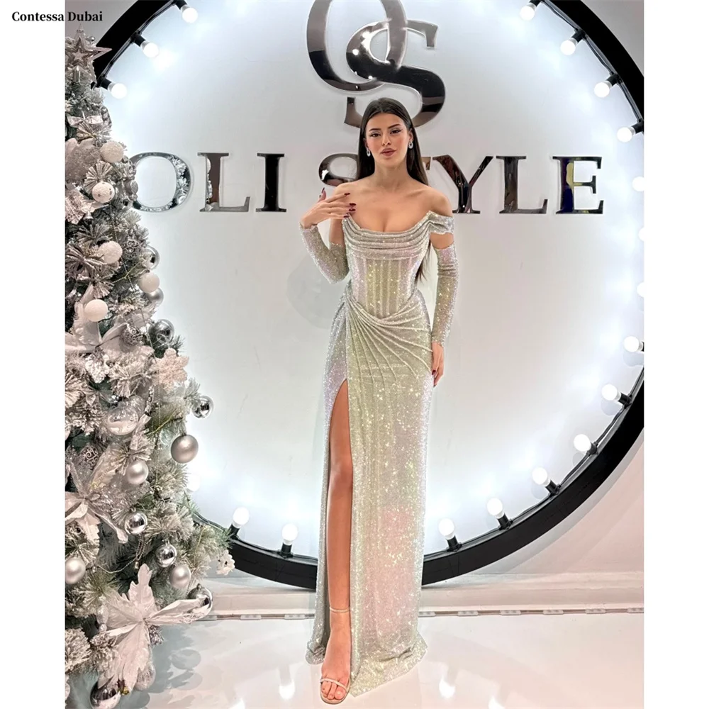 ชุดราตรีสีเงินเงา Contessa Dubai สำหรับงานพรอม แขนยาวเปิดไหล่ ผ่าข้างสูง ชุดราตรีออกงานอย่างเป็นทางการ ปี 2025
